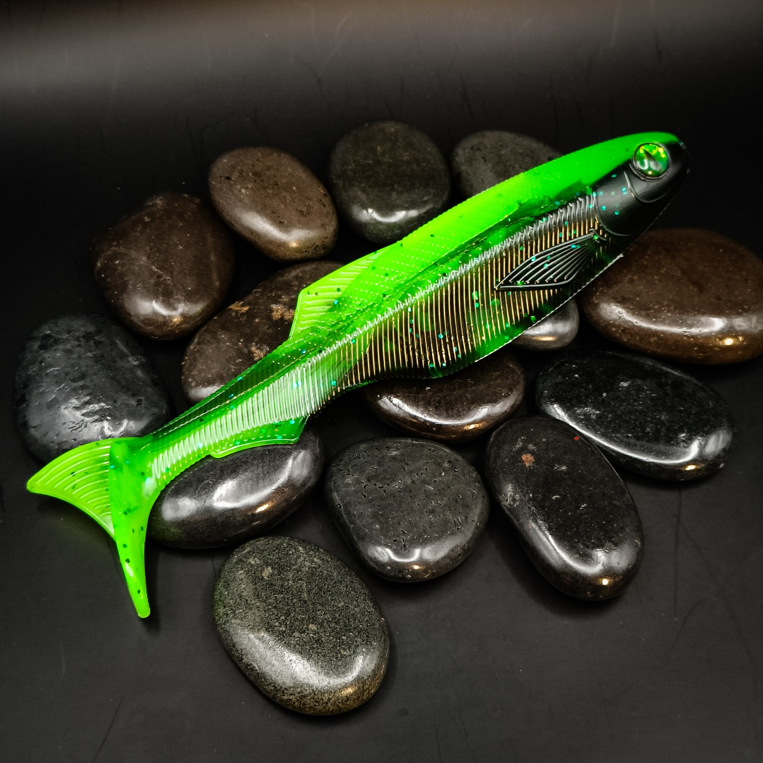 Toxic Waste Scrapper 19.2 cm in bright green and black with glitter and a green eye, displayed on dark pebbles.